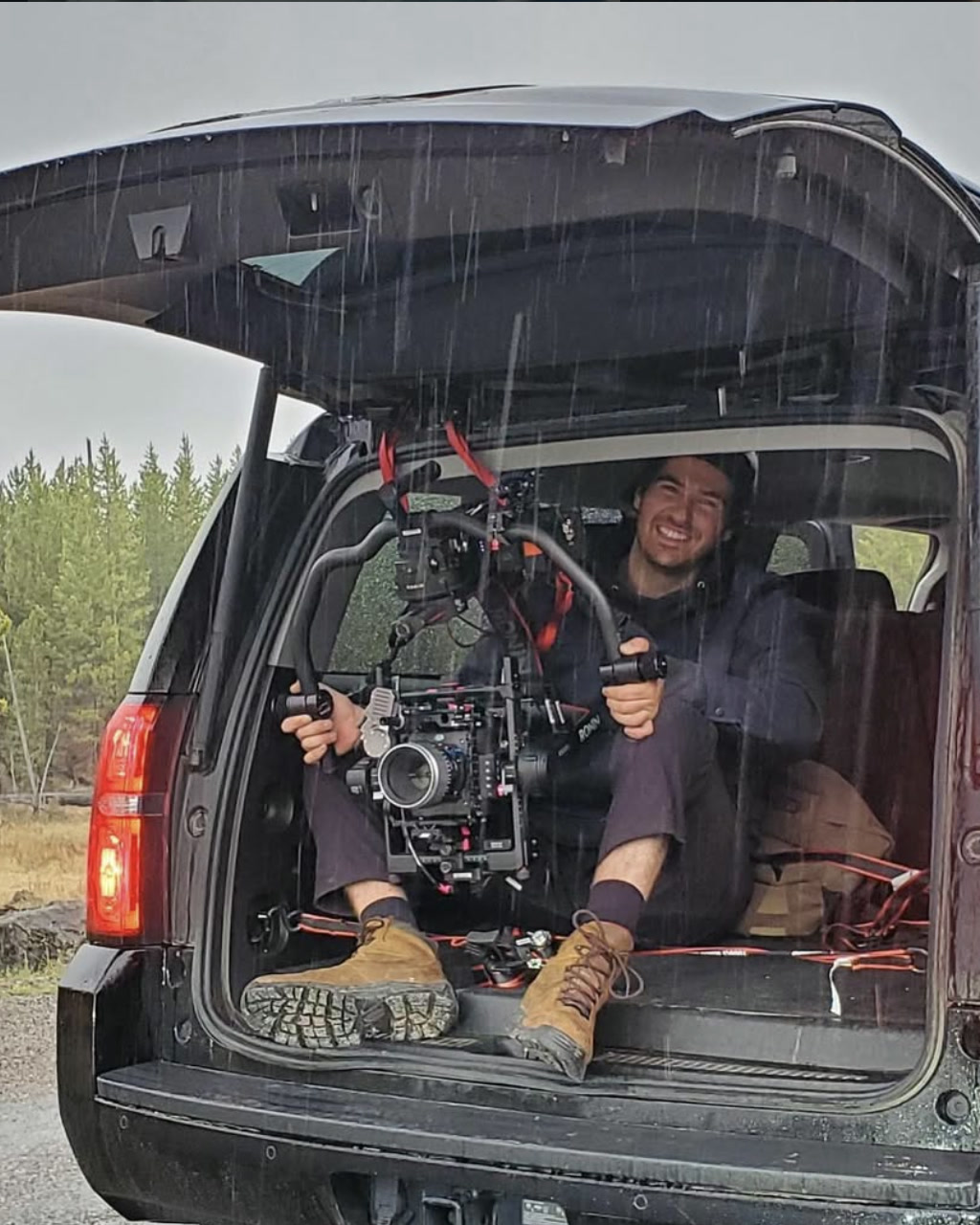 Adam Linssen smiling with a cinema camera during a rainy location shoot