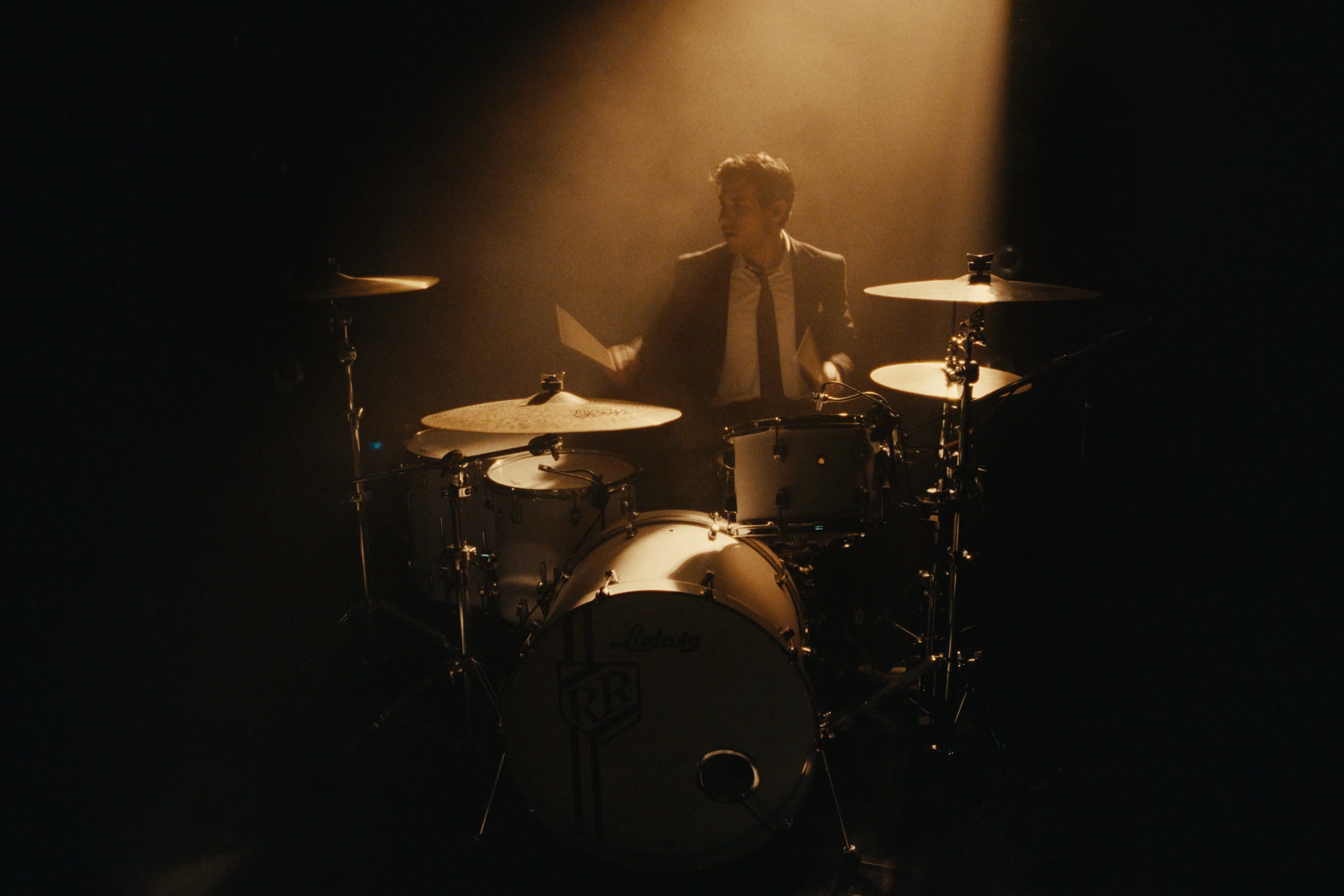 A drummer silhouetted in a focused amber spotlight